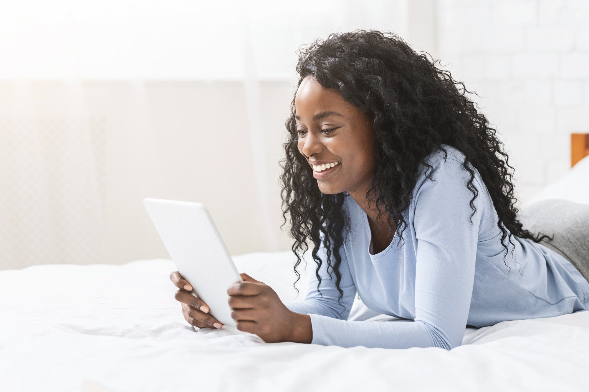 Girl reading blog on digital tablet in bed