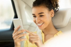Happy woman using smartphone, sitting on back seat in car