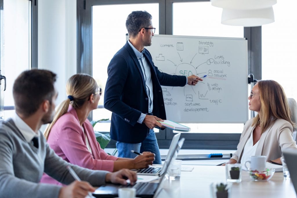 handsome businessman pointing at white blackboard and explain a project to her colleagues