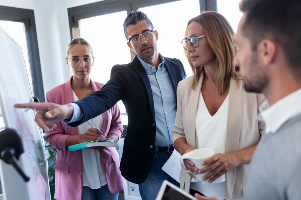 Handsome businessman pointing at white blackboard and explain a project to her colleagues