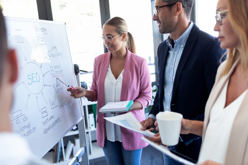 young businesswoman pointing at white blackboard and explain a project to her colleagues